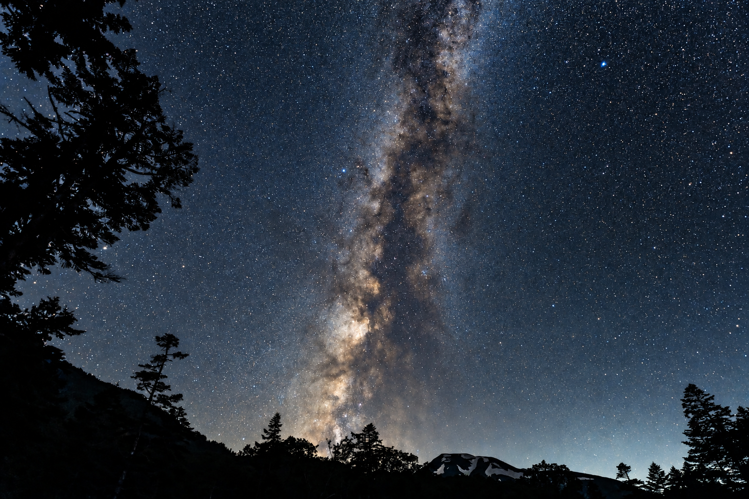 The Milky Way over a dark mountain and forest